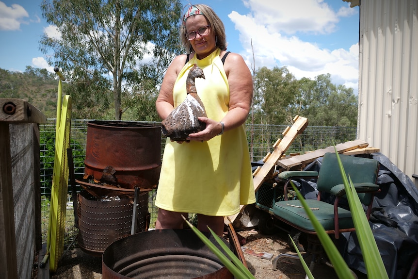 A woman in front of a drum kiln holding a ceramic bird