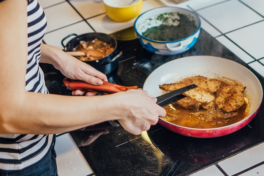 Woman using induction stove to cook chicken close up