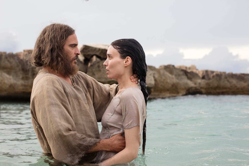 Colour still image from 2018 film Mary Magdalene of Joaquin Phoenix and Rooney Mara standing waist deep in water by the coast.