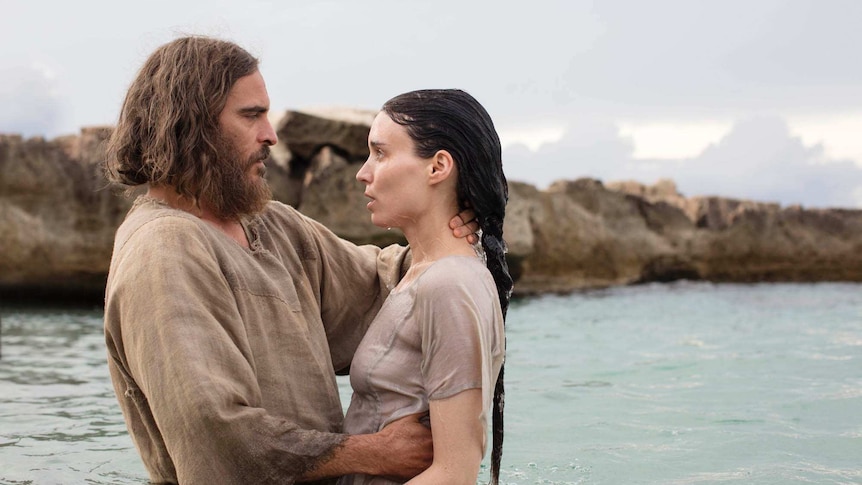 Colour still image from 2018 film Mary Magdalene of Joaquin Phoenix and Rooney Mara standing waist deep in water by the coast.