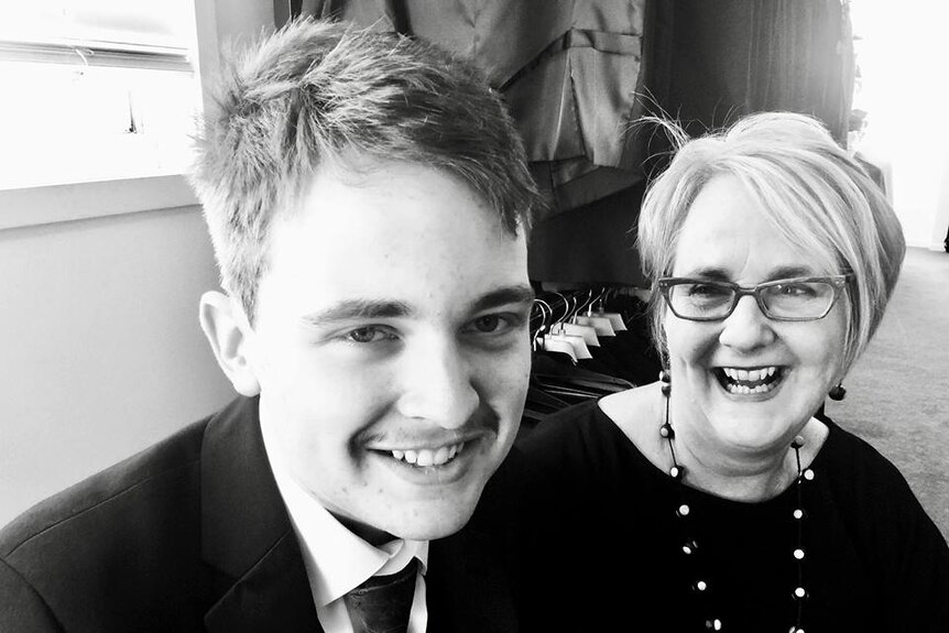 teenage boy sits alongside mum in a suit shop, she is smiling looking at him and he is smiling looking at the camera.