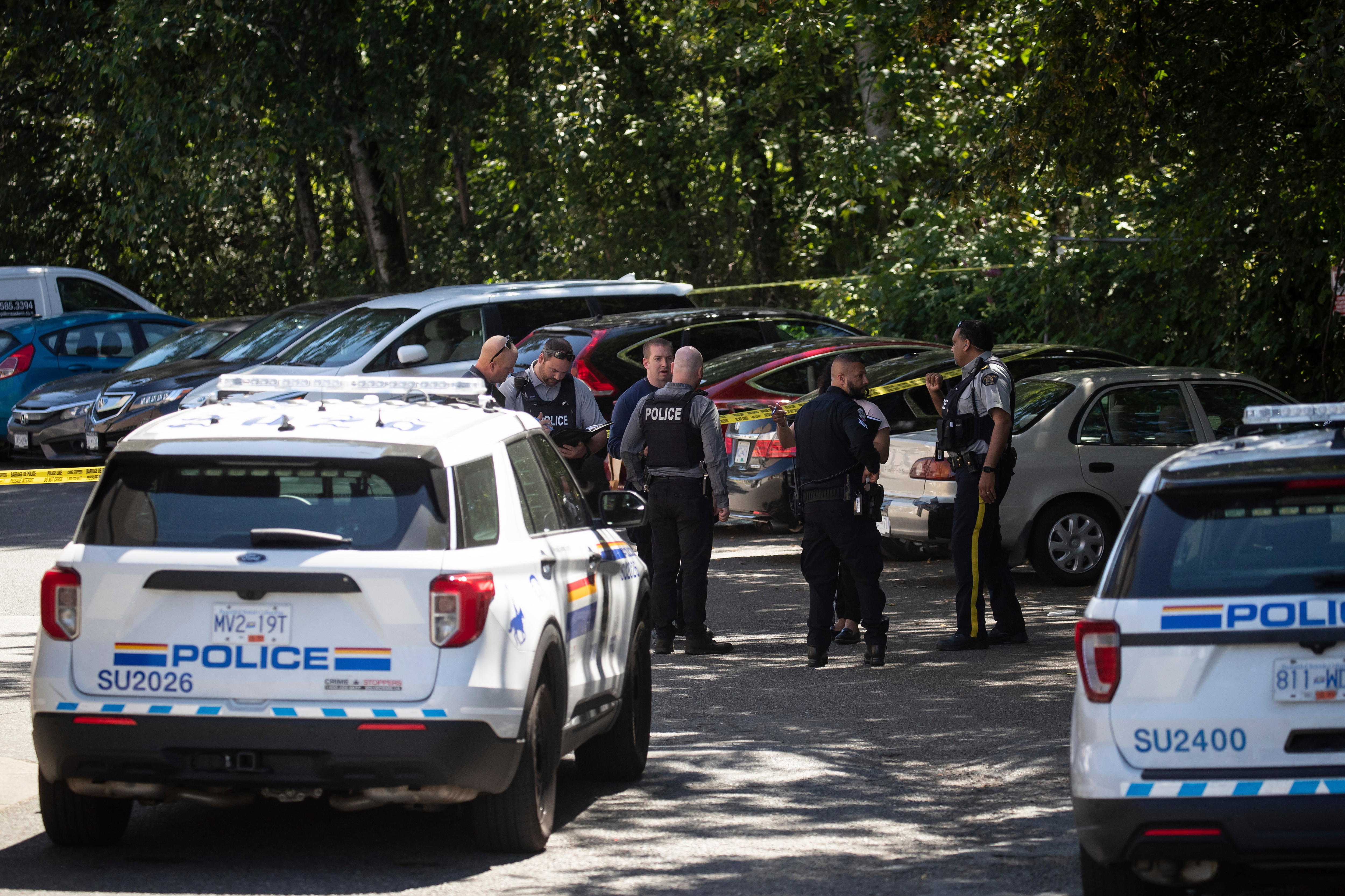 Canadian police officers stand in a circle talking in a parking lot at the crime scene of Ripudaman Singh Malik's shooting. 