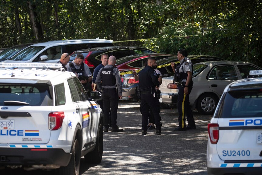 Canadian police officers stand in a circle talking in a parking lot at the crime scene of Ripudaman Singh Malik's shooting. 