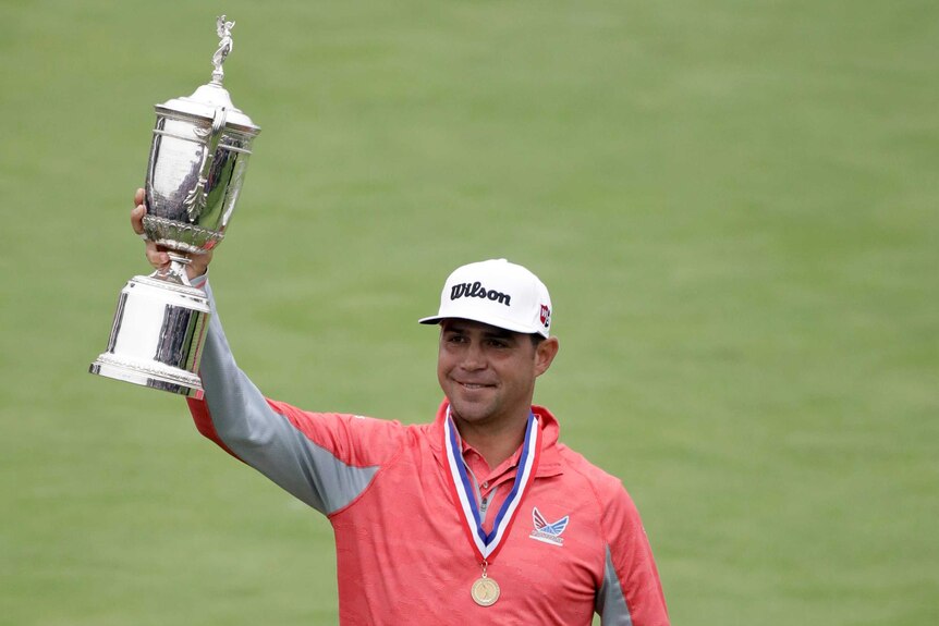 Gary Woodland holds up the US Open trophy wearing a medal around his neck with a red white and blue ribbon