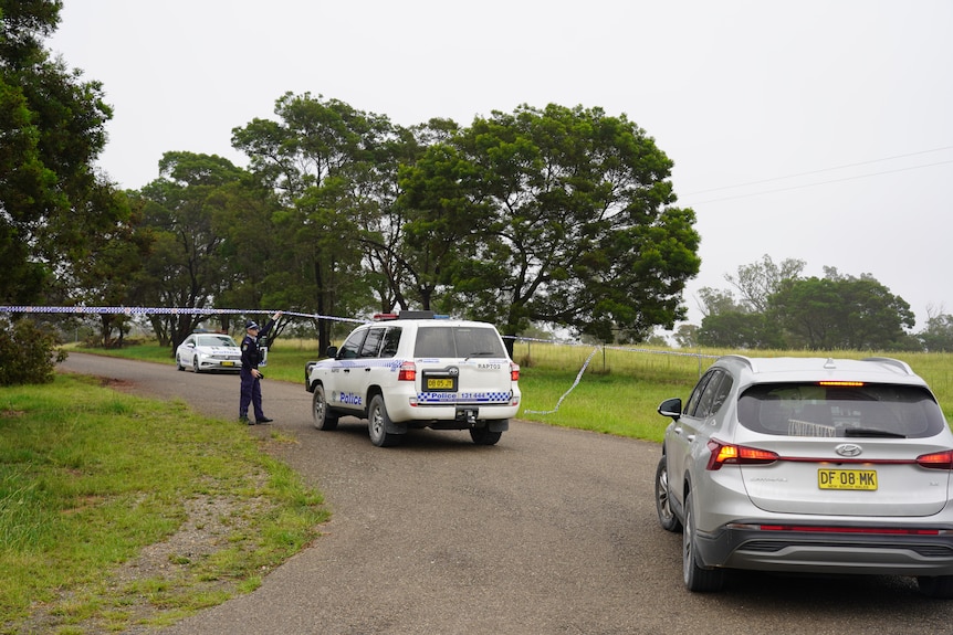NSW Police officers and vehicles at property in Bungonia, officer lifts police tape to allow a four-wheel drive under