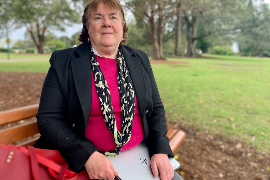 Woman sitting on a park bench, holding a laptop.