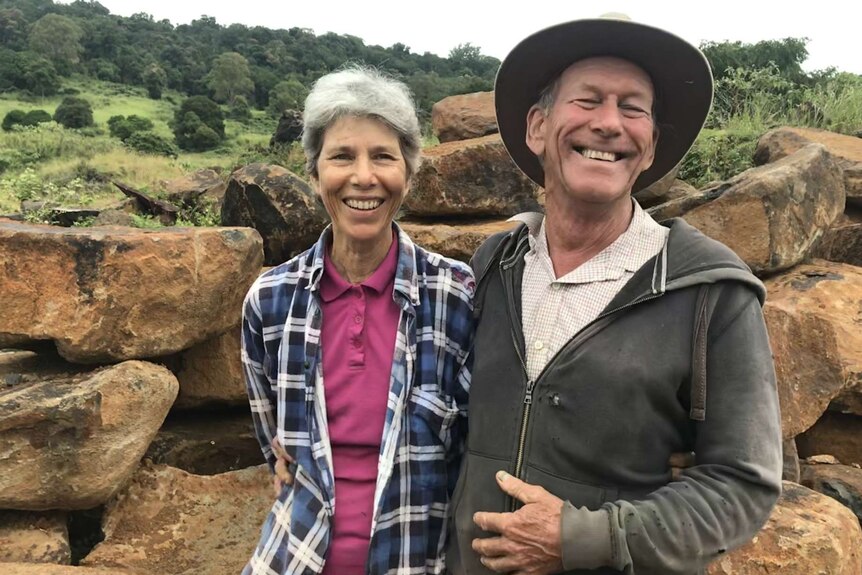 Carol smiling and Ian laughing as they stand in front of their rocks.