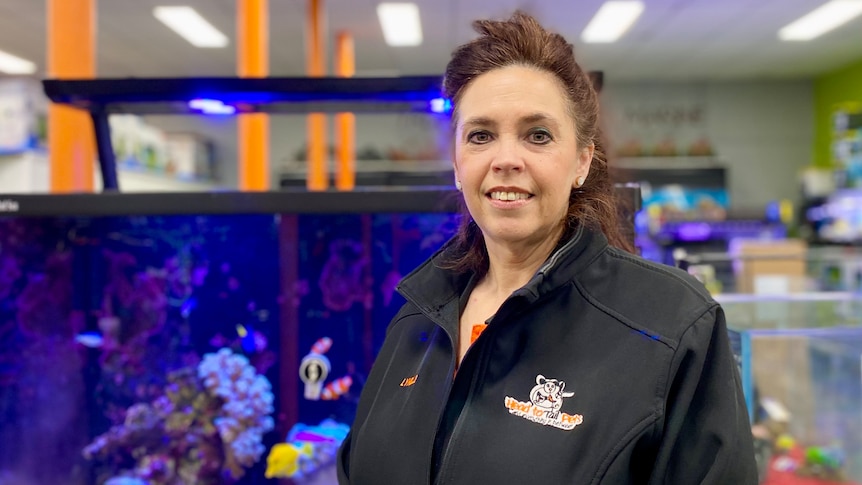 Woman stands in front of a fish tank inside a pet shop.