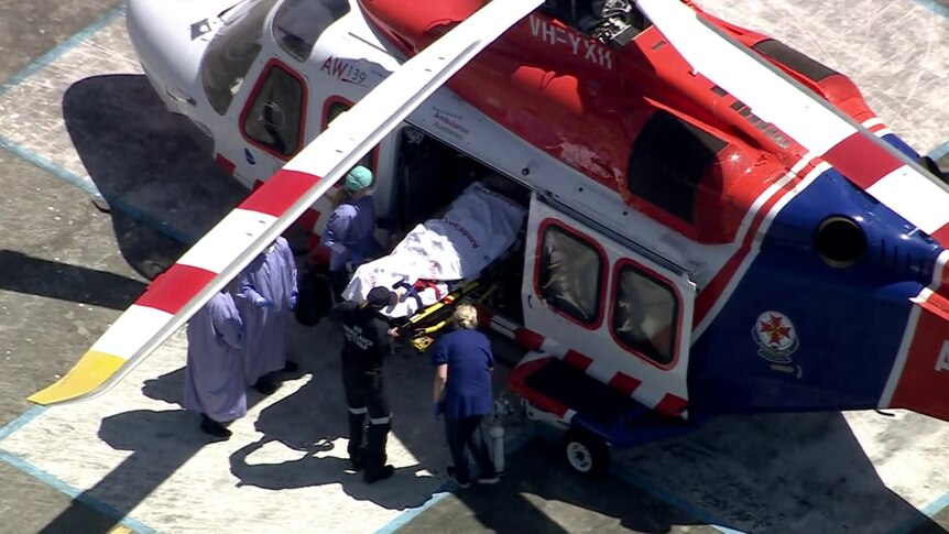 An overview of the lower half of a person being carried out of an air ambulance on a stretcher, surrounded by medical staff.