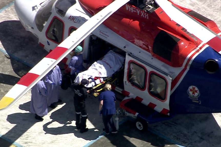 An overview of the lower half of a person being carried out of an air ambulance on a stretcher, surrounded by medical staff.