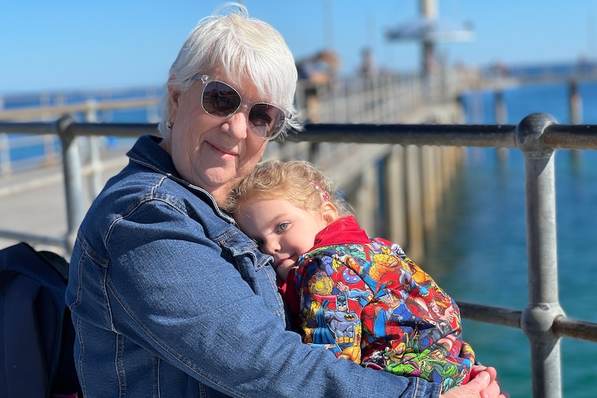 An elderly woman wearing sunglasses while holding a child at a jetty