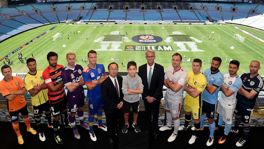 The captains of the A-League clubs pose in a line with a young boy and two men in suits.