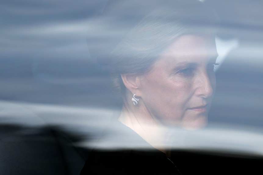 A photo of a sophisticated woman through a foggy car windscreen, staring vacantly dressed in black  