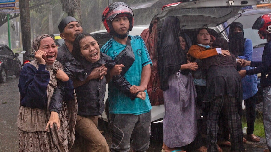 Women cry in despair as a body is recovered in the rain from under the rubble.