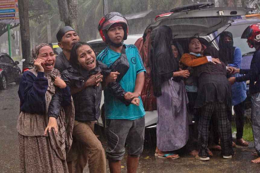 Women cry in despair as a body is recovered in the rain from under the rubble.