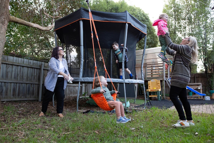 Sharon and Bec and their three children jump on the trampoline and play in the backyard.