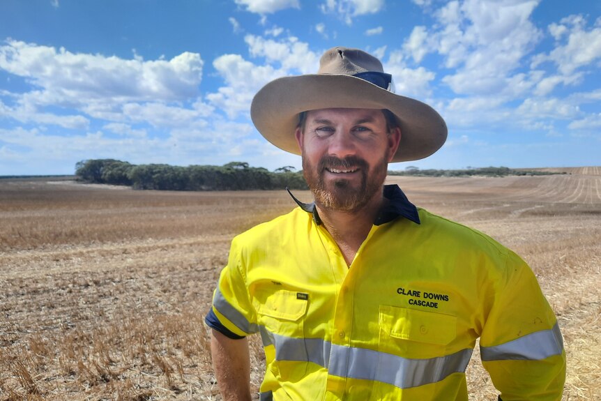 He wears a hat and high-vis and stands in a paddock