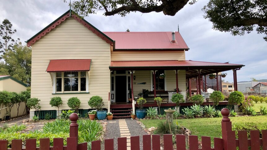 An old Queenslander with a verandah and lots of potted plants around it.