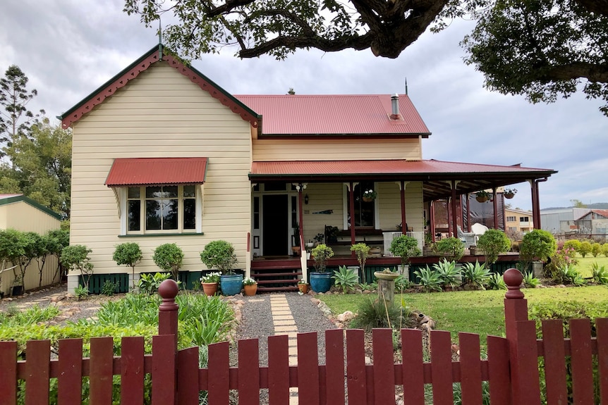 A gorgeous old Queenslander with a verandah and lots of potted plants around it.