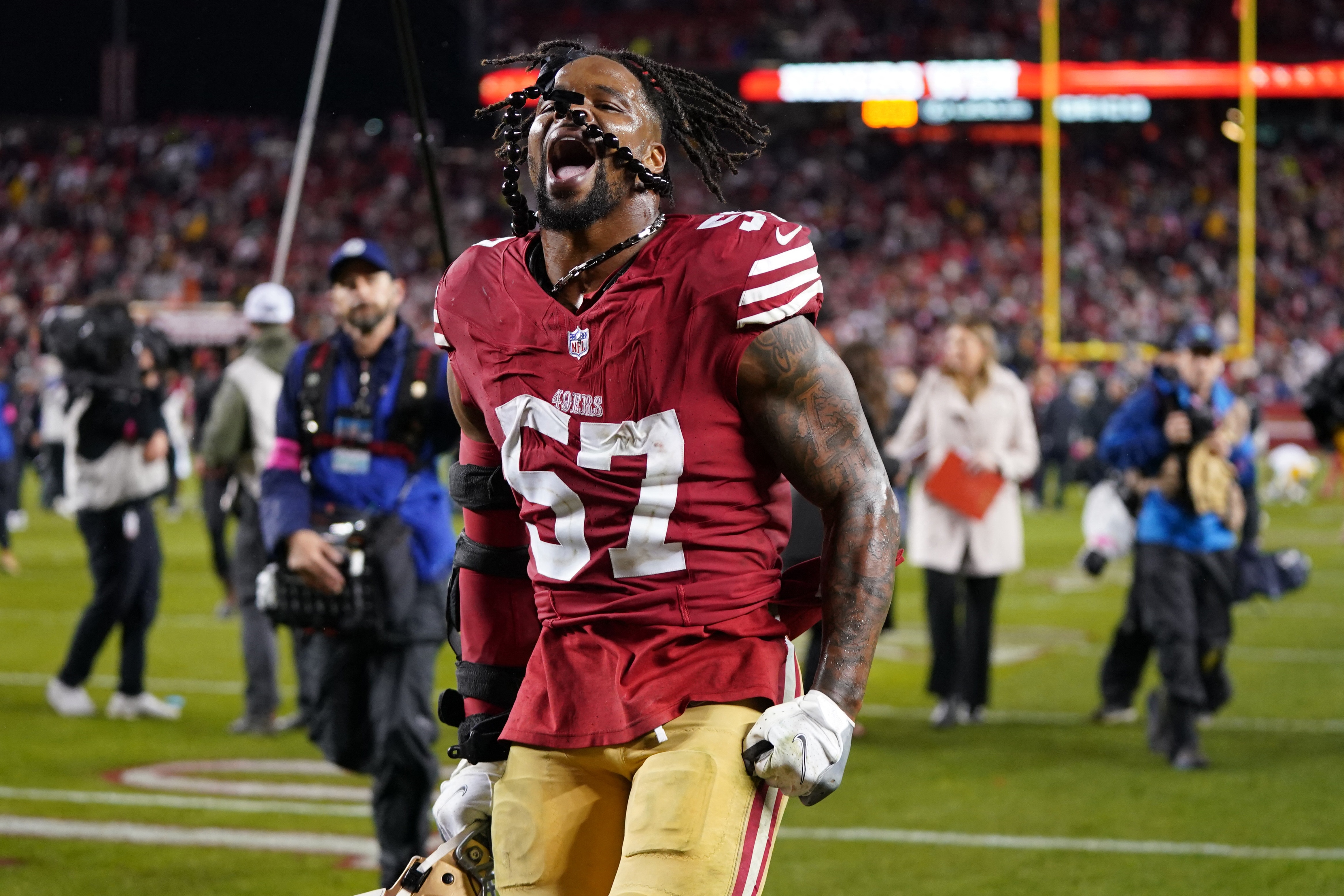 An NFL player in red, jumping and celebrating as he runs off the field following victory. 