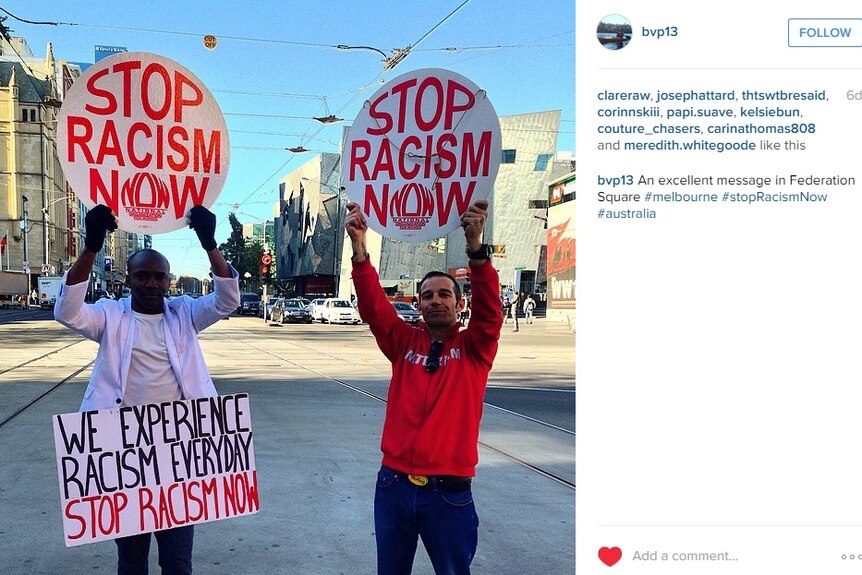 Two men hold signs reading "stop racism now"