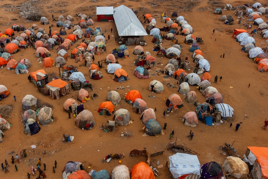 An aerial shot shows lots of bright orange tent-like structures in a dry, dusty landscape