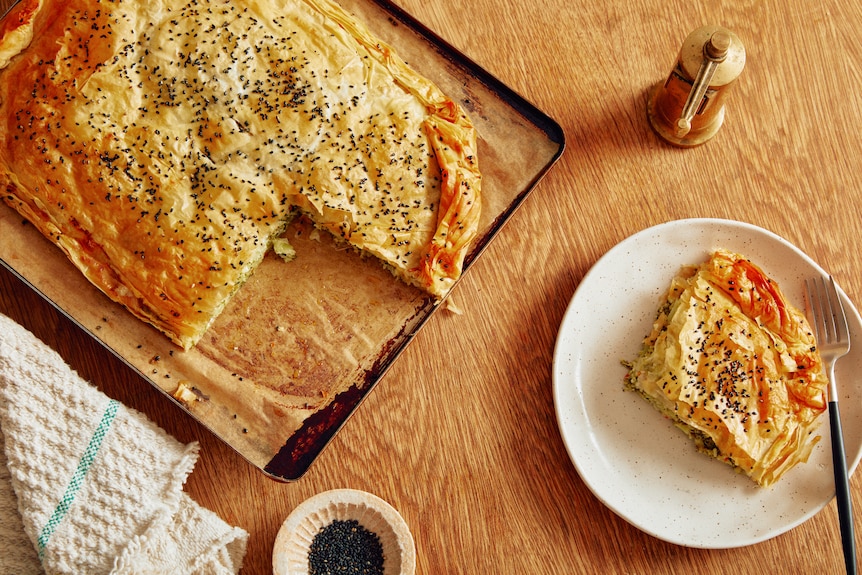 A freeform pie, made with filo pastry, sits on a baking tray with a slice removed. It has a broccoli, feta and halloumi filling.