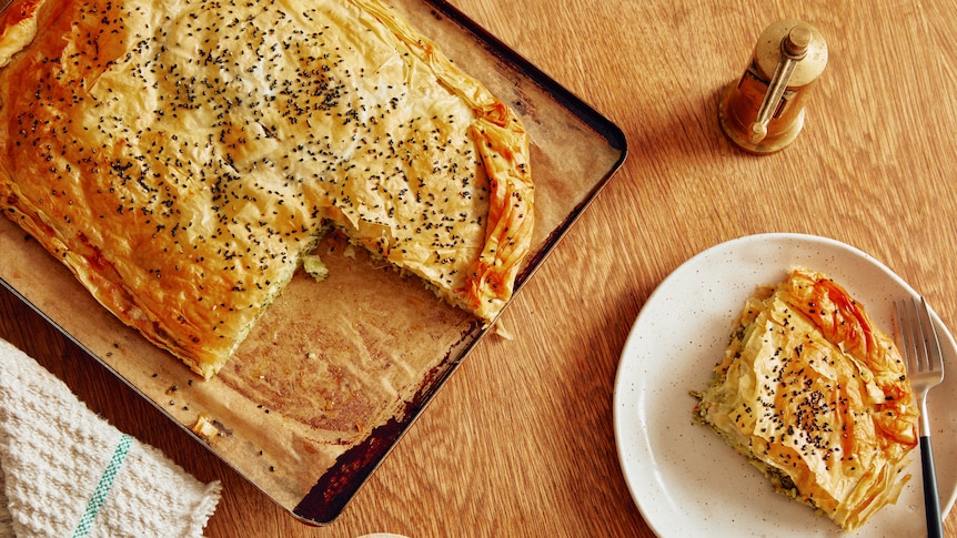 A freeform pie, made with filo pastry, sits on a baking tray with a slice removed. It has a broccoli, feta and halloumi filling.
