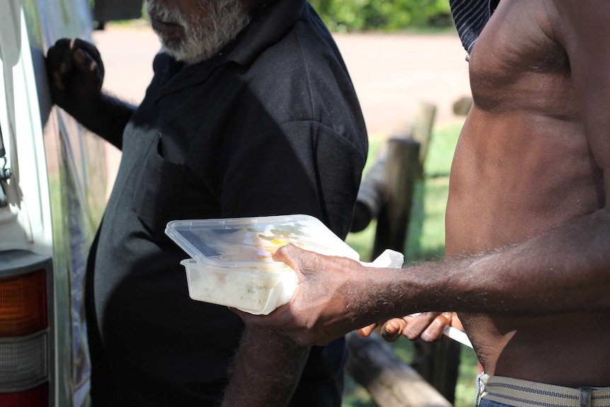 A man hands out a plastic container of food to another man.
