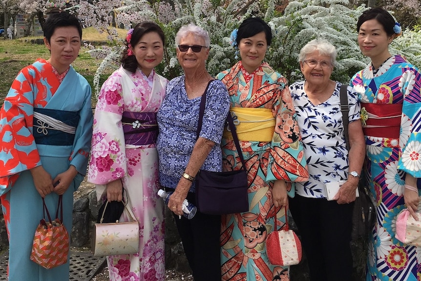 Japanese women in kimono stand with two older Australian women under a cherry blossom tree.