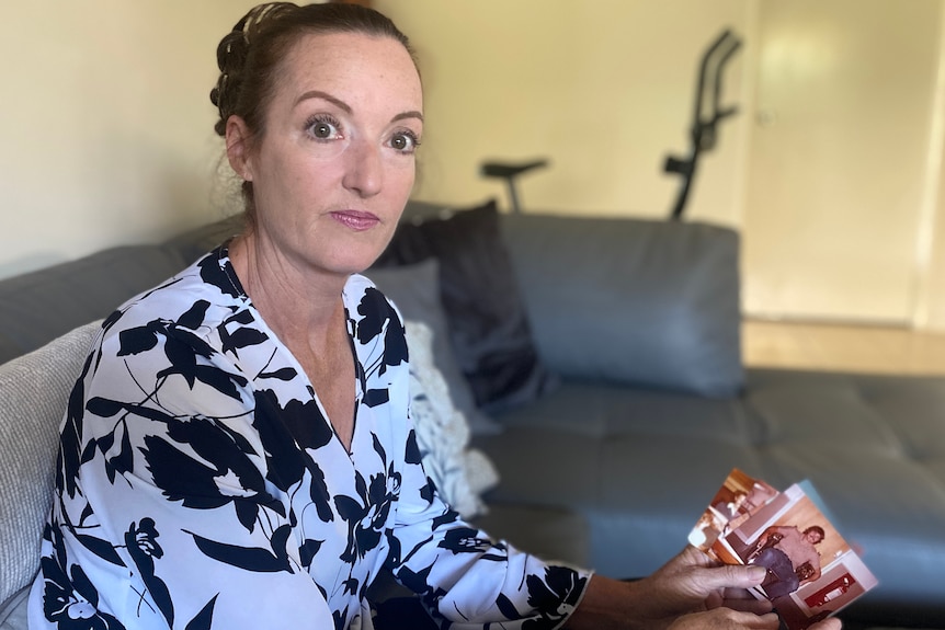 A woman sitting on a couch looking up, while holding several photos in her hands. 