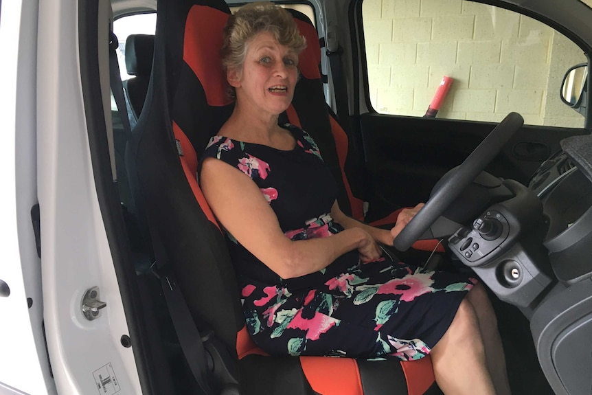 A woman sits in a modified driver's seat of a car with the door open, looking at the camera.