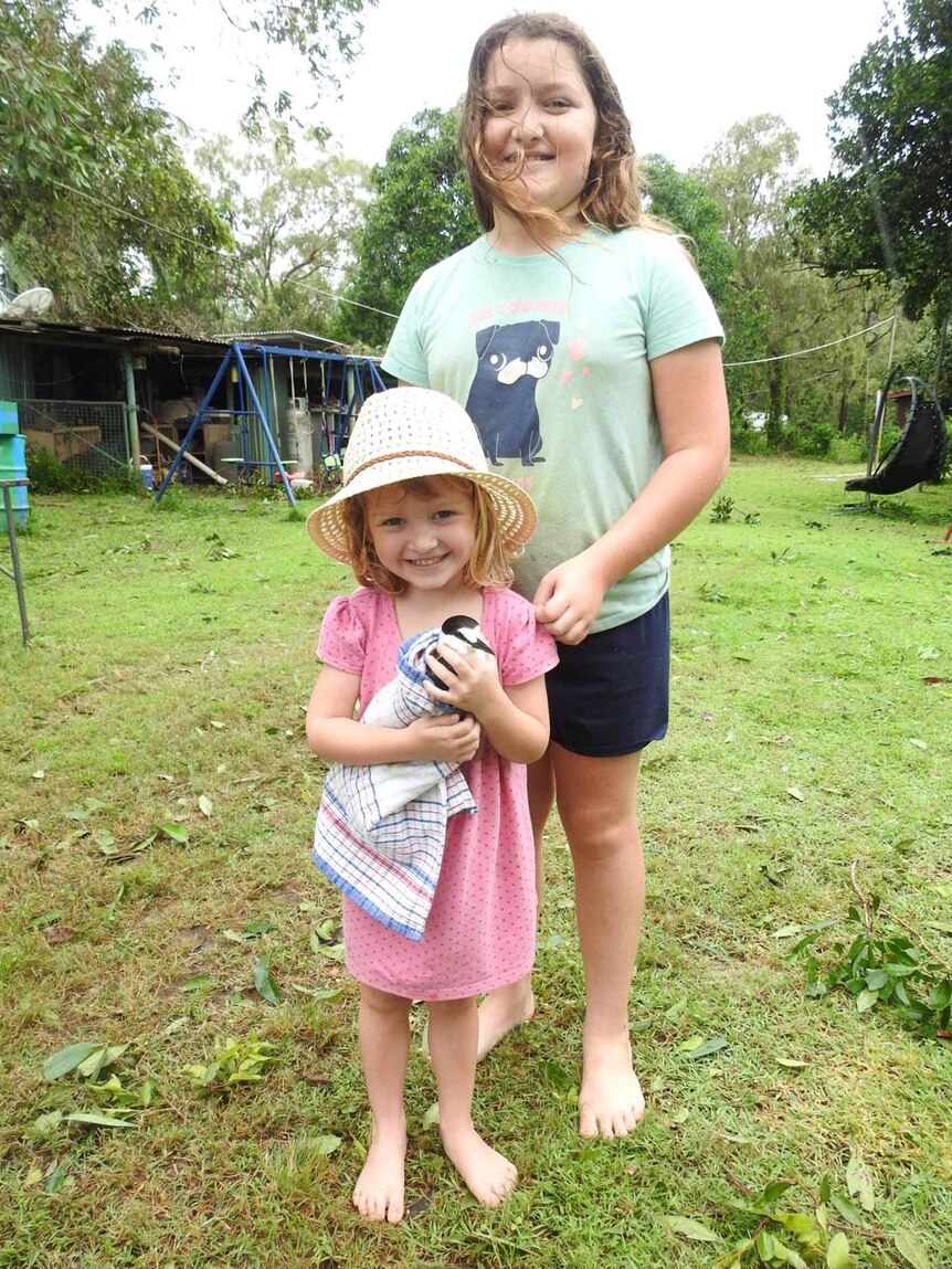 Two sisters on an outback property, the younger girl holding an injured bird