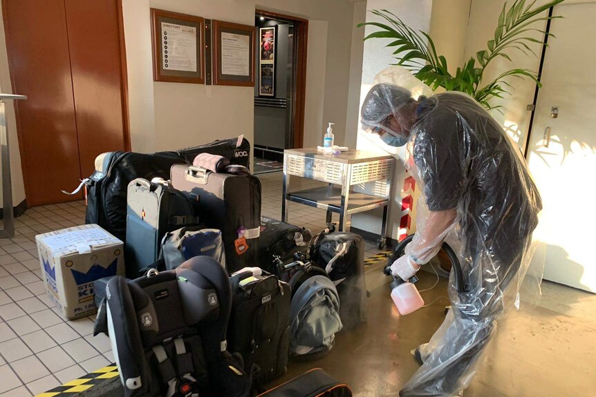 A man wearing a protective suit and face mask sprays down luggage in a lobby.
