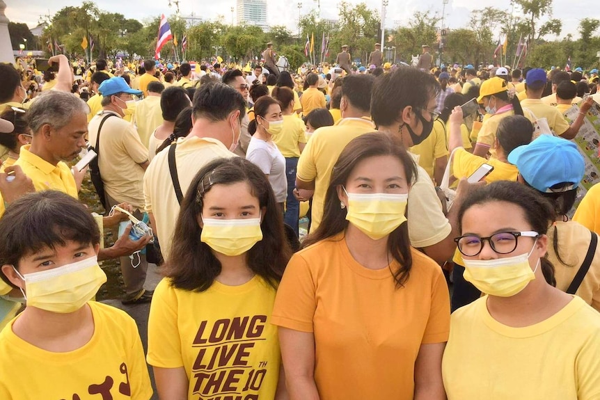 A woman with three girls wearing masks and yellow shirts stand in front of a crowd of people wearing yellow.