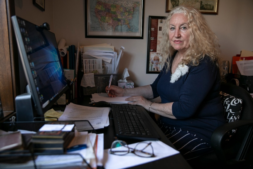 a woman with white curly hair sits at desk