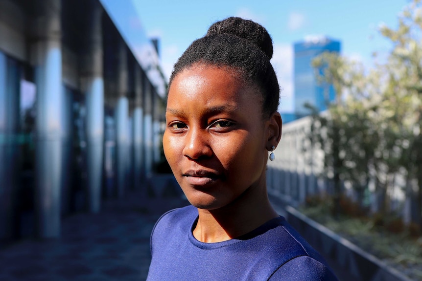 Nasilele wearing blue top, hair in a bun, standing on a city office balcony.