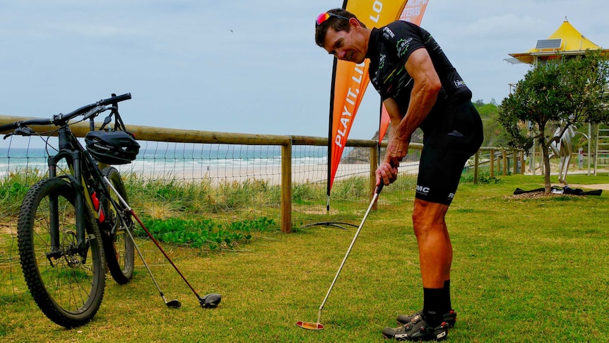 Man hits golf ball with mountain bike in the background