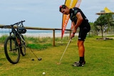 Man hits golf ball with mountain bike in the background