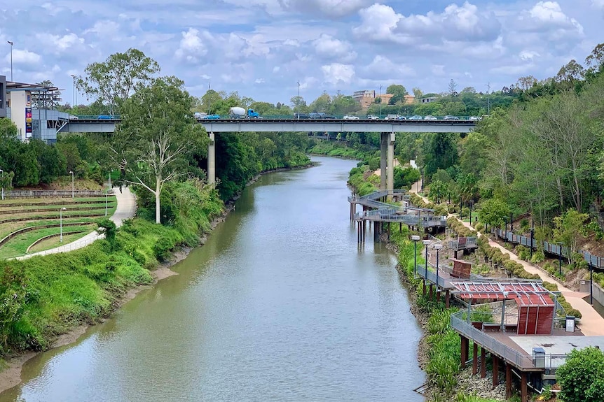 A high road bridge passing over a river with walkways along its steep banks