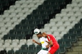 Two footballers compete for the ball in an empty stadium.