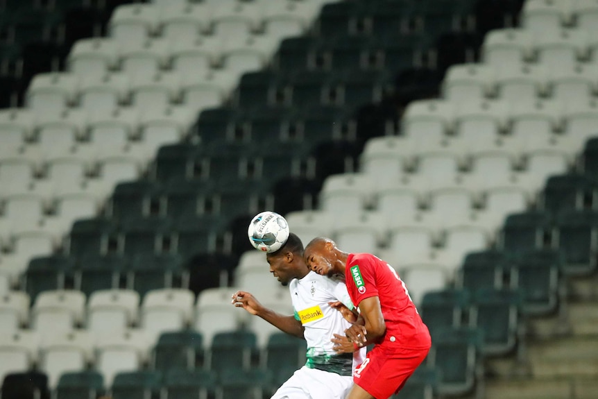 Two footballers compete for the ball in an empty stadium.