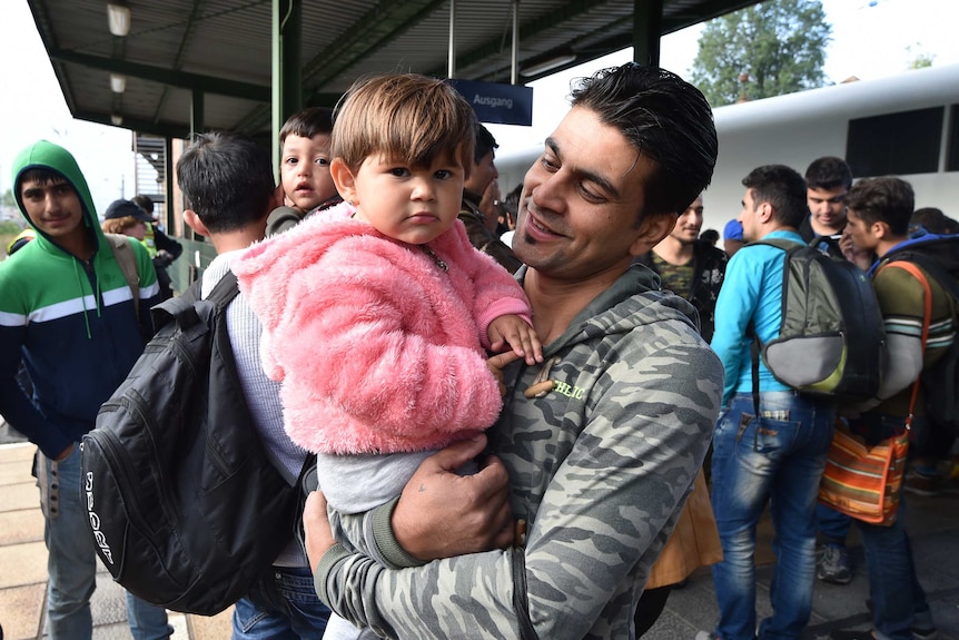 A man holds a child as they get out of a train