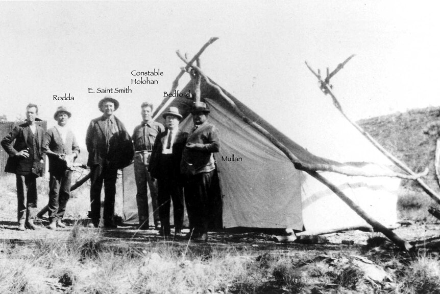 A small group of men stand in front of a white tent.