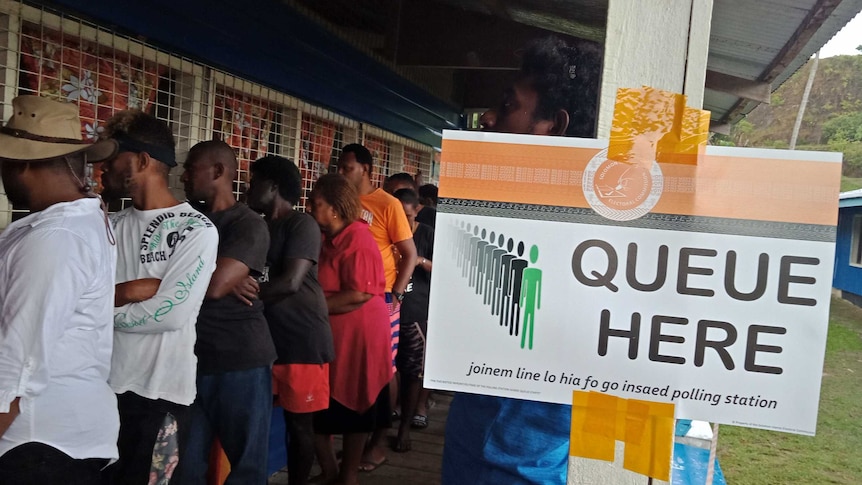 A line of voters wait next a to a sign directing people where to vote.