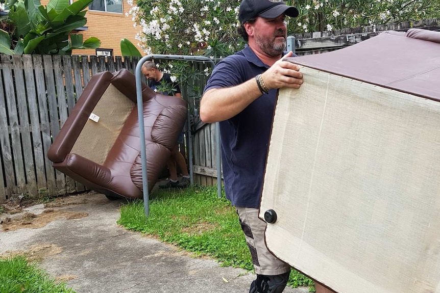 Two men carry sofas into a house
