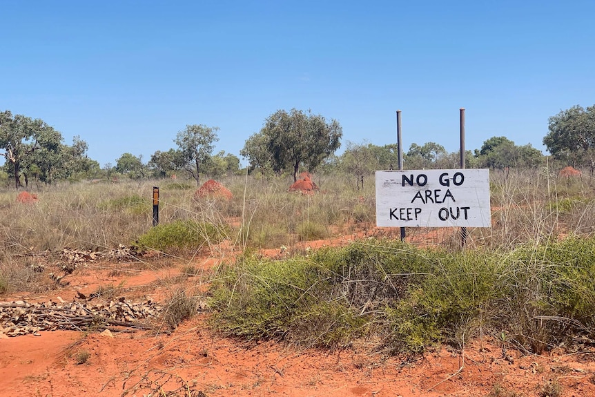 Image of a sign in front of thick bush and grassland, the sign says 'no go area, keep out.'