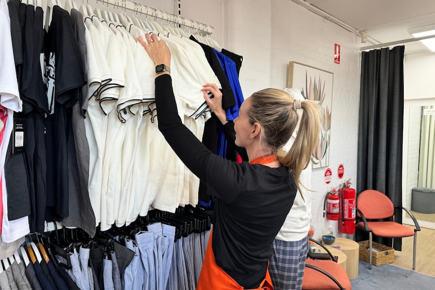 服装店里的一名妇女正在整理挂在墙上的衣服。