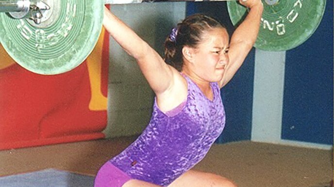 Erika Yamasaki lifts a barbell with weights at a competition as a young weightlifter, date and location unknown.