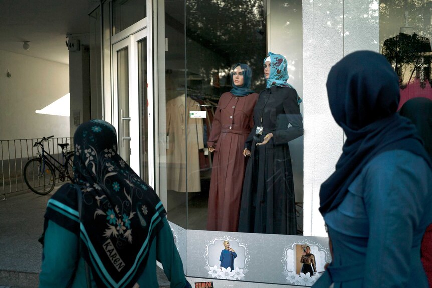 Women wearing hijabs walk past a window showing women wearing hijabs.